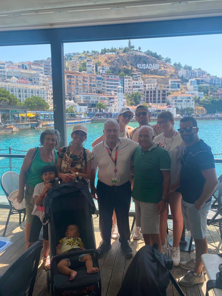 Celebrity Infinity guests meeting their licensed guide Nedret Güngör at the start of a private Ephesus tour, on the Starbucks terrace at Kuşadası cruise port with the KUŞADASI hillside sign behind them, 28 July 2026